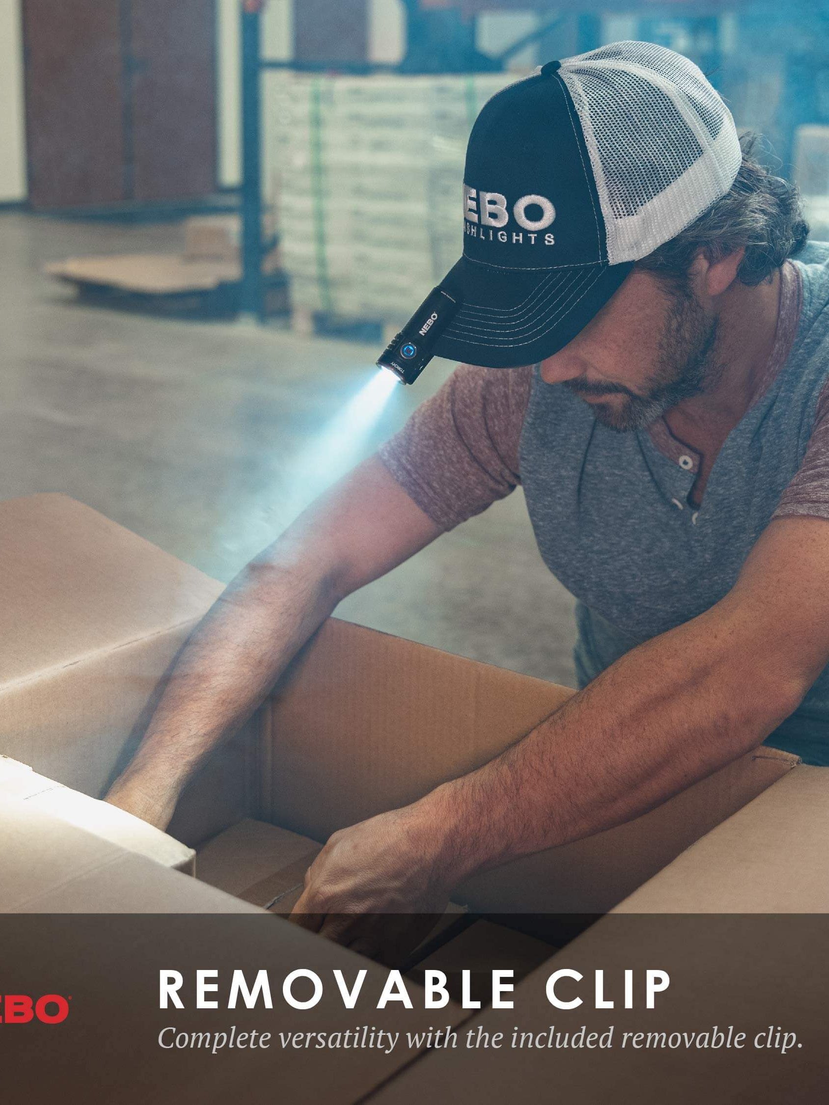 Man using NEBO flashlight with removable clip, showcasing versatility in a dimly lit workspace.