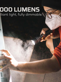 Person using NEBO Slyde King flashlight with spray can, showcasing 2000 lumens brightness in a dimmable setting.