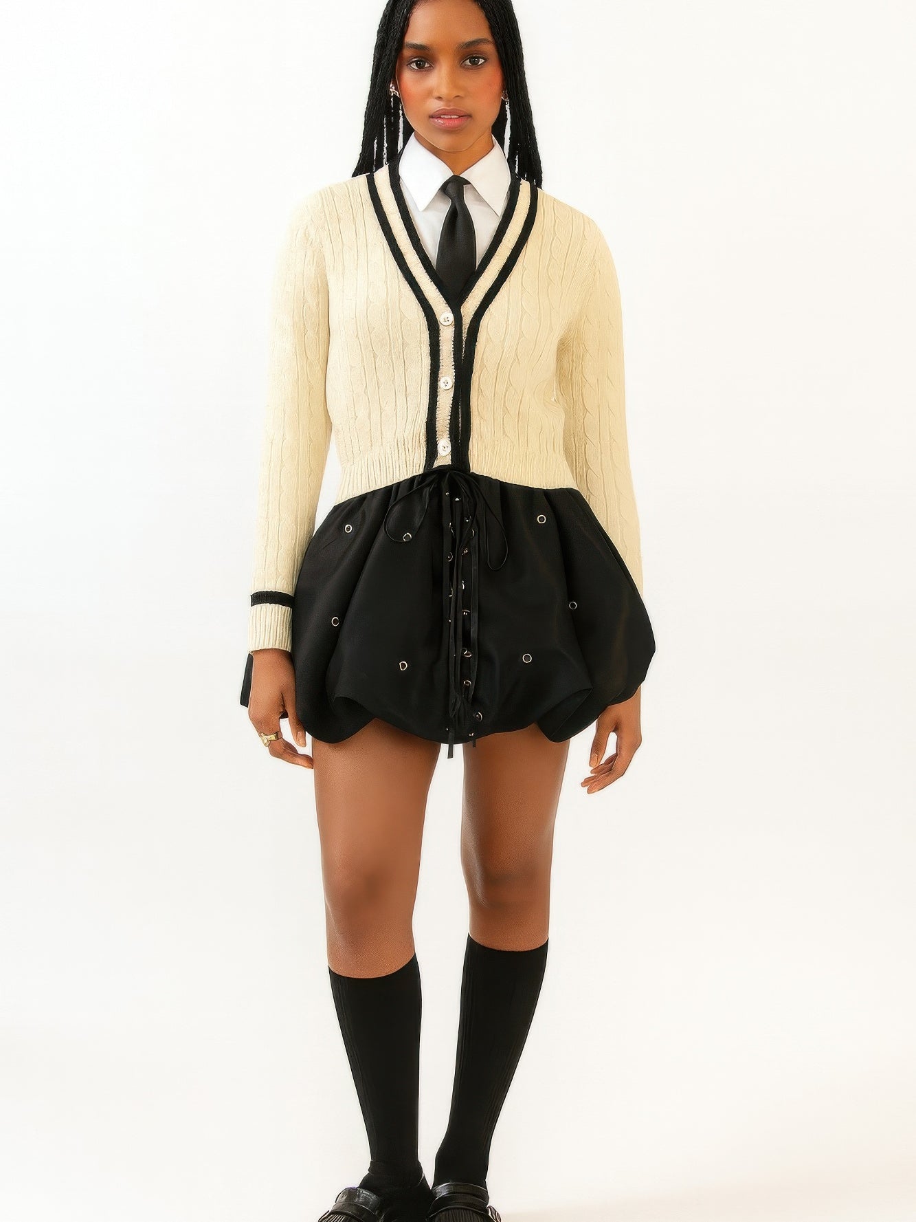 Model wearing a Bubble Lace Up Mini Skirt paired with a sweater and tie. Stylish outfit showcasing trendy design.