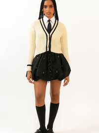 Model wearing a Bubble Lace Up Mini Skirt paired with a sweater and tie. Stylish outfit showcasing trendy design.