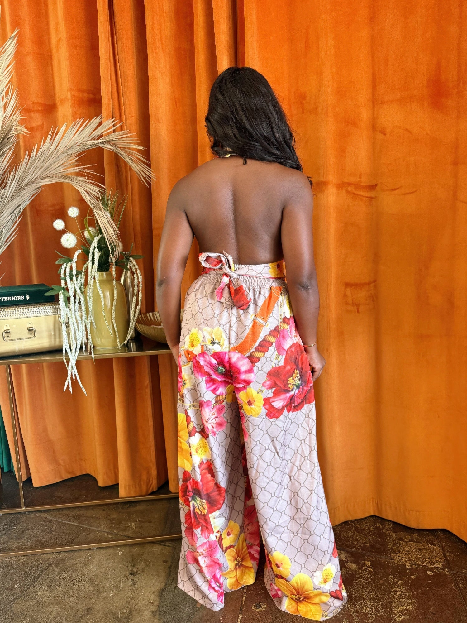 Back view of a woman wearing a Paradise Bloom Jumpsuit, showcasing its resort style jumpsuit features and floral print.