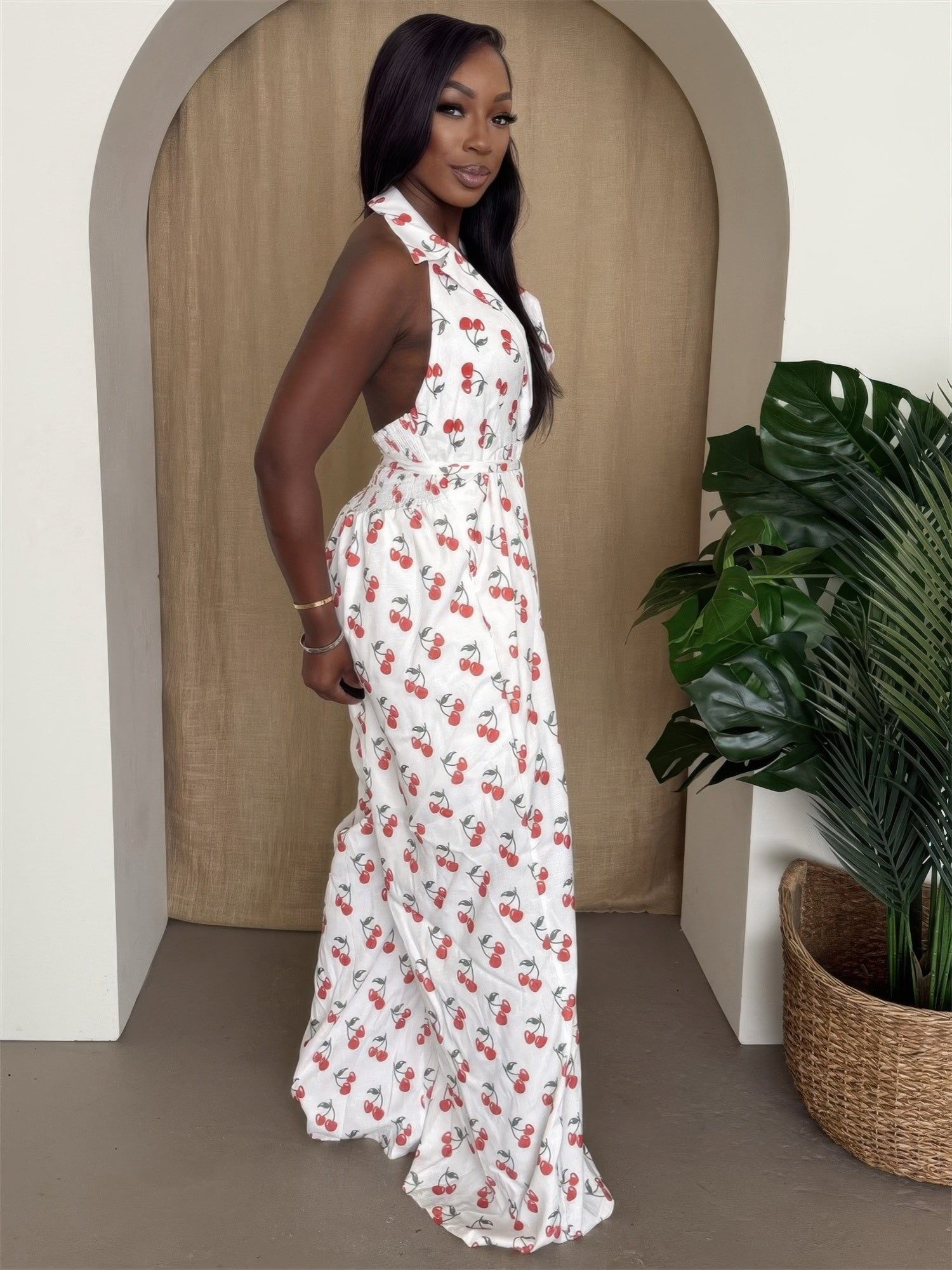 Model showcasing the cherry print jumpsuit with a halter neckline and wide-leg pants, surrounded by greenery.