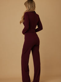 Side view of a woman wearing a burgundy blazer jumpsuit for women with long sleeves and a cinched waist.