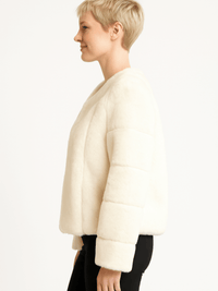 Side view of a woman wearing a cozy, ivory faux fur jacket with a relaxed fit and long sleeves.