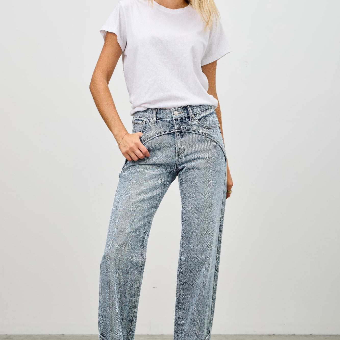 Woman wearing Mid Rise Straight With Piping jeans with a white t-shirt and heels against a plain background.