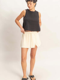 Model wearing a wrap front elastic waist skort paired with a black sleeveless top and sandals.