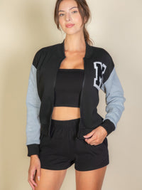 Model wearing a Letter Patched Striped Trim Varsity Jacket with bold "M" logo, paired with a black crop top and shorts.