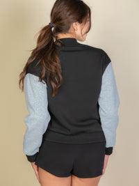 Back view of a woman wearing a black and gray striped trim varsity jacket with a stylish ponytail.