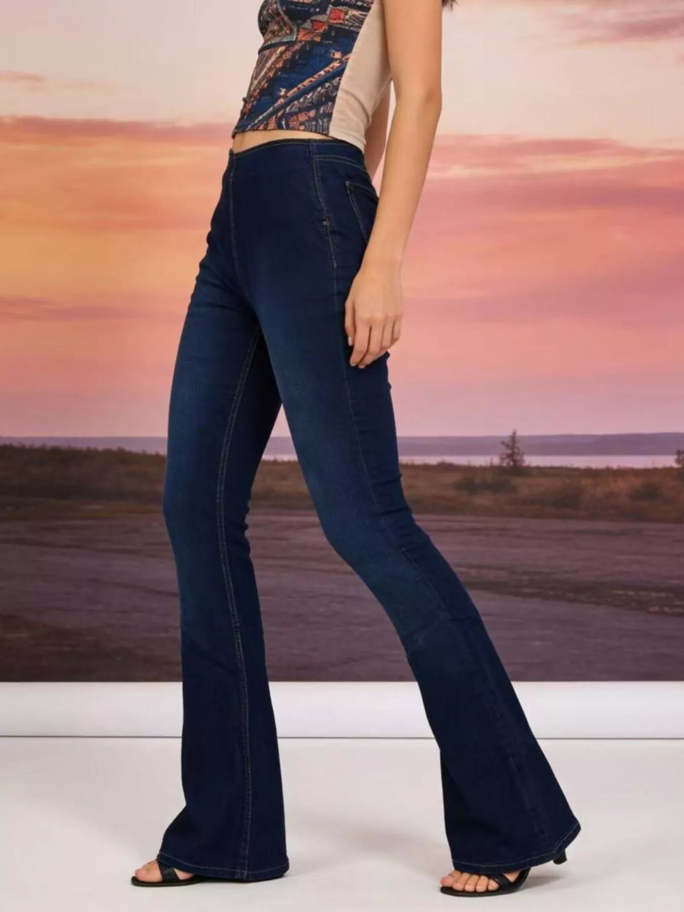 High-Waisted Flare Jeans showcased in dark wash, styled with a trendy top against a sunset background.