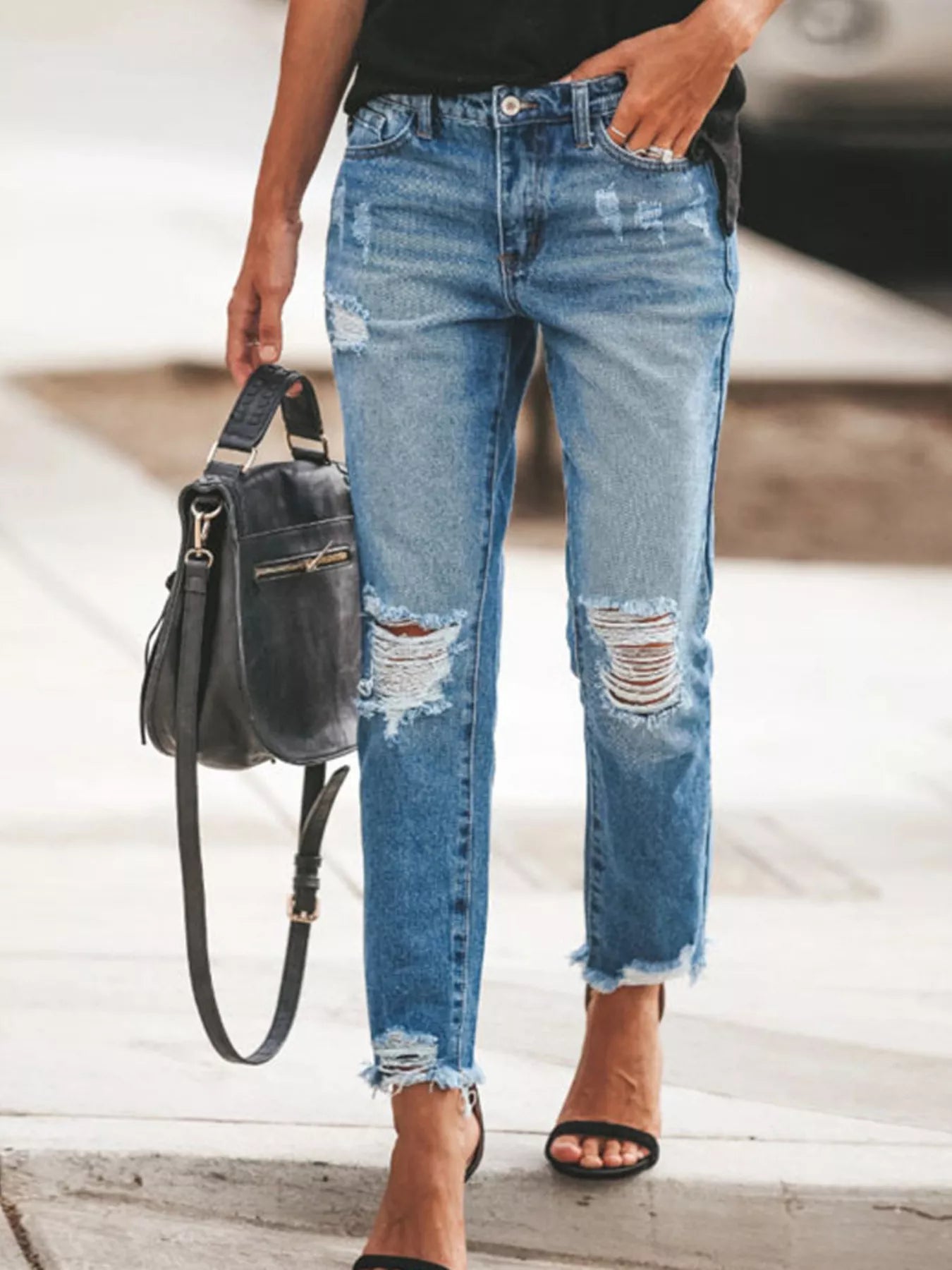 Model wearing Distressed Wash Ankle Jeans while holding a black handbag on a city street.