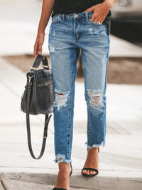 Model wearing Distressed Wash Ankle Jeans while holding a black handbag on a city street.