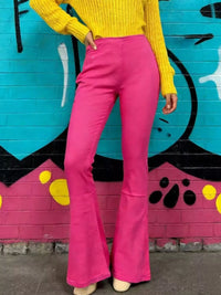 Model wearing High-Waisted Flare Jeans in pink with a yellow sweater against a colorful mural background.