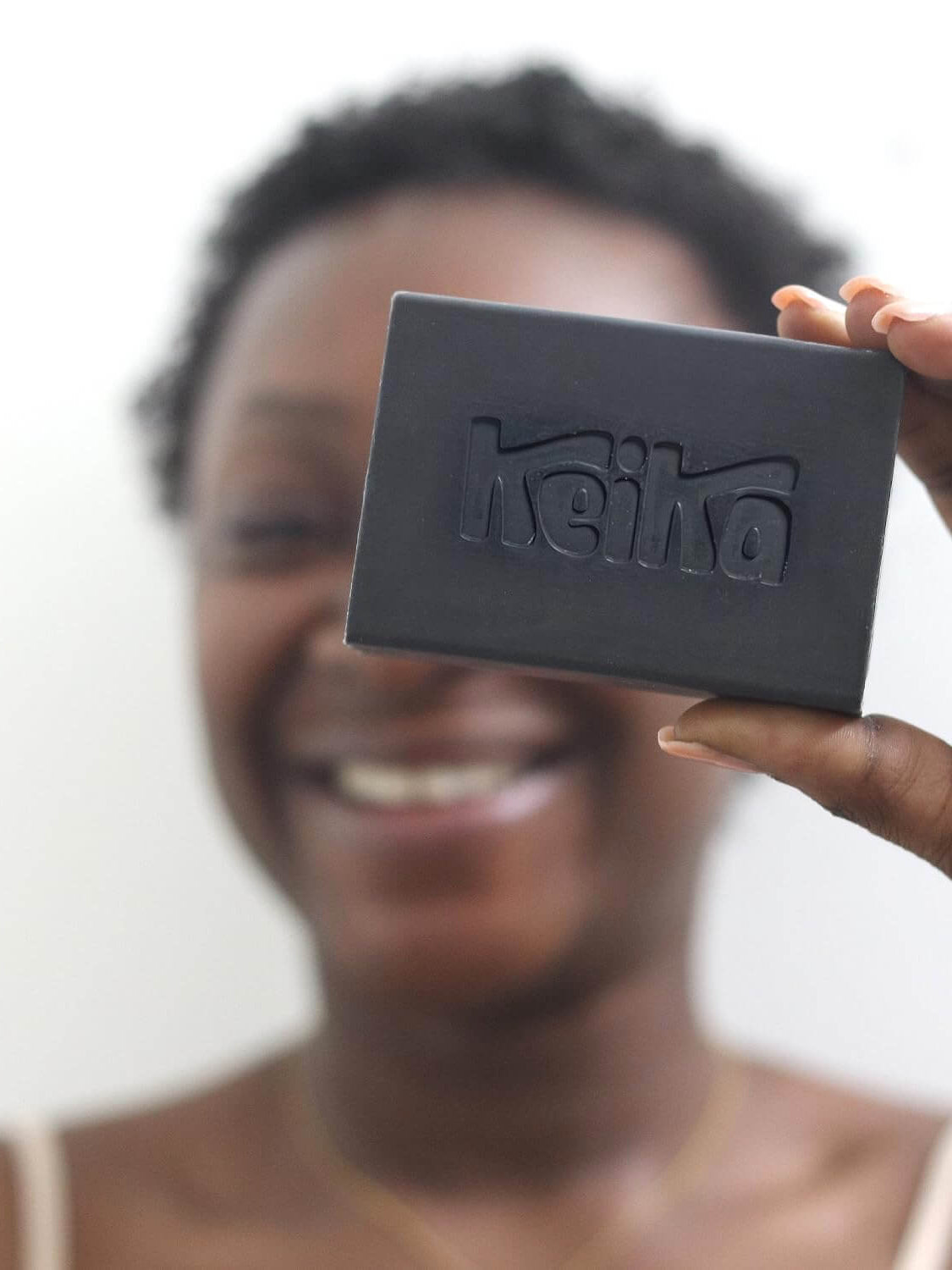 Smiling woman holding Keika Charcoal Black Soap Bar, ideal for eczema and oily skin care.