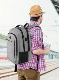 Man wearing a MATEIN Travel Laptop Backpack in austere grey, standing at a train station.