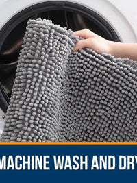 Person holding a soft grey chenille bath rug near a washing machine, indicating it's machine washable and dryable.