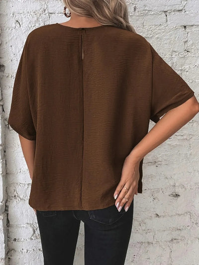 Knotted Round Neck Half Sleeve Blouse in brown, showcasing a relaxed fit and back detail against a textured wall.