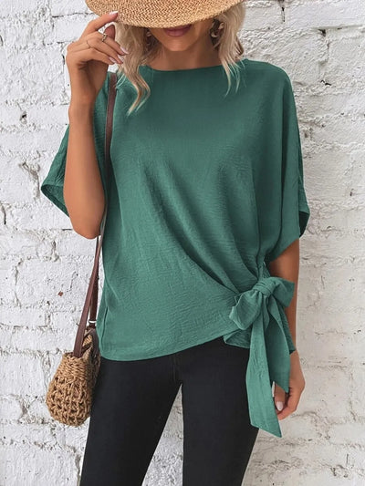 Knotted Round Neck Half Sleeve Blouse in green, styled with a straw hat and crossbody bag, showcasing the tied detail.