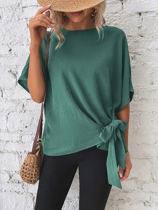 Knotted Round Neck Half Sleeve Blouse in green, styled with a straw hat and crossbody bag, showcasing the tied detail.
