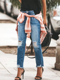 Distressed Wash Ankle Jeans with raw hem, styled with a plaid shirt and heels on a city street.