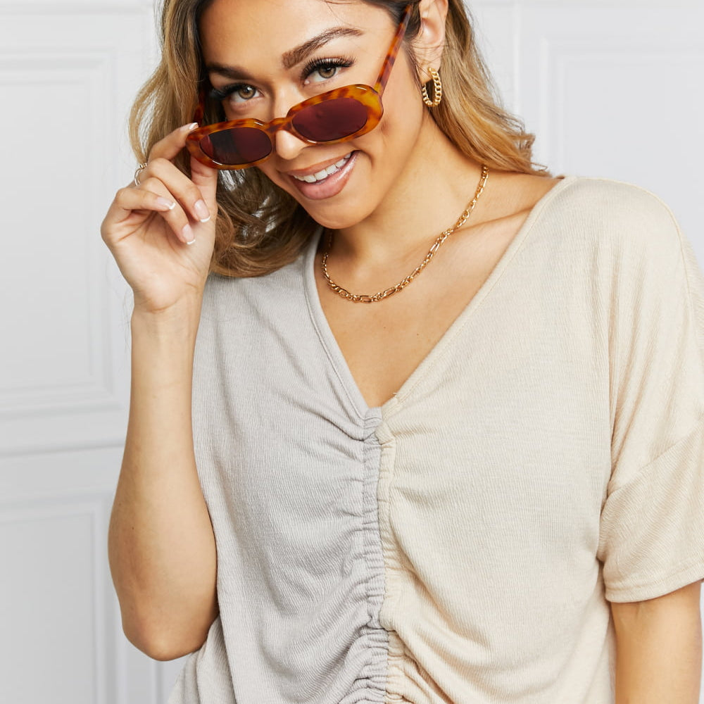 Oval Full Rim Sunglasses worn by a smiling woman in a stylish top, showcasing trendy eyewear.