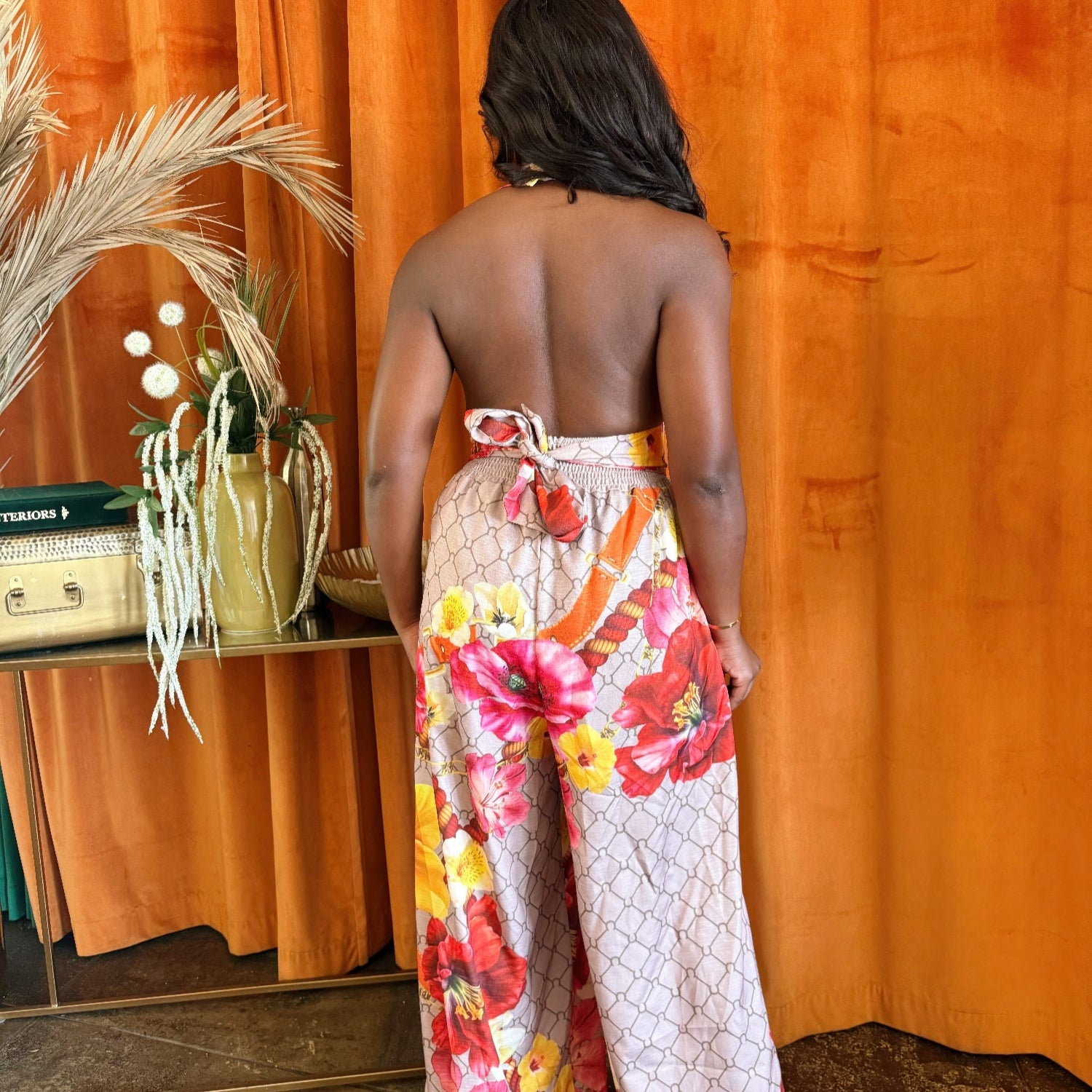 Back view of a woman wearing a Paradise Bloom Jumpsuit, showcasing its resort style jumpsuit features and floral print.