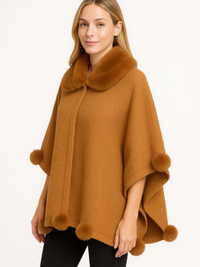 Woman wearing a stylish trim cape with faux fur collar and pom trim in a warm color.