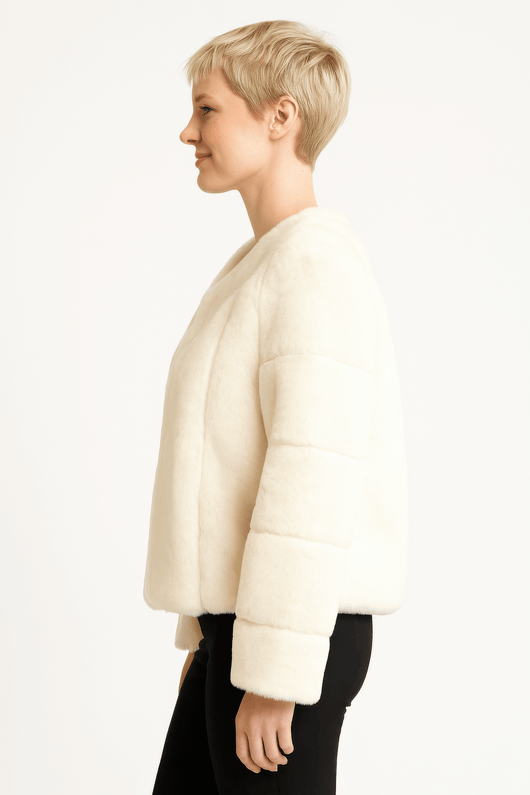 Side view of a woman wearing a cozy, ivory faux fur jacket with a relaxed fit and long sleeves.