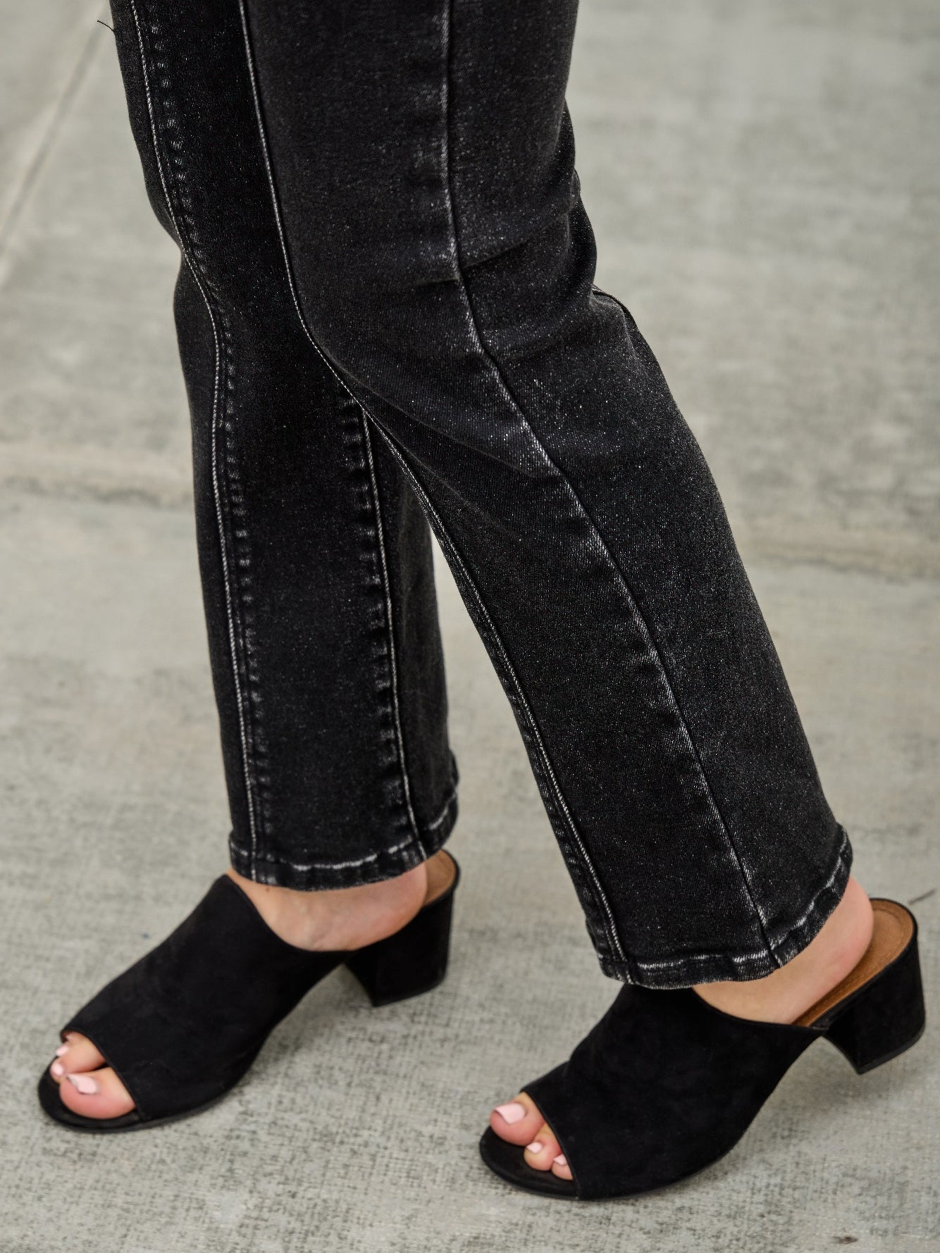 Person wearing Mid Rise Slim Straight In Black Acid jeans with black open-toe mules.