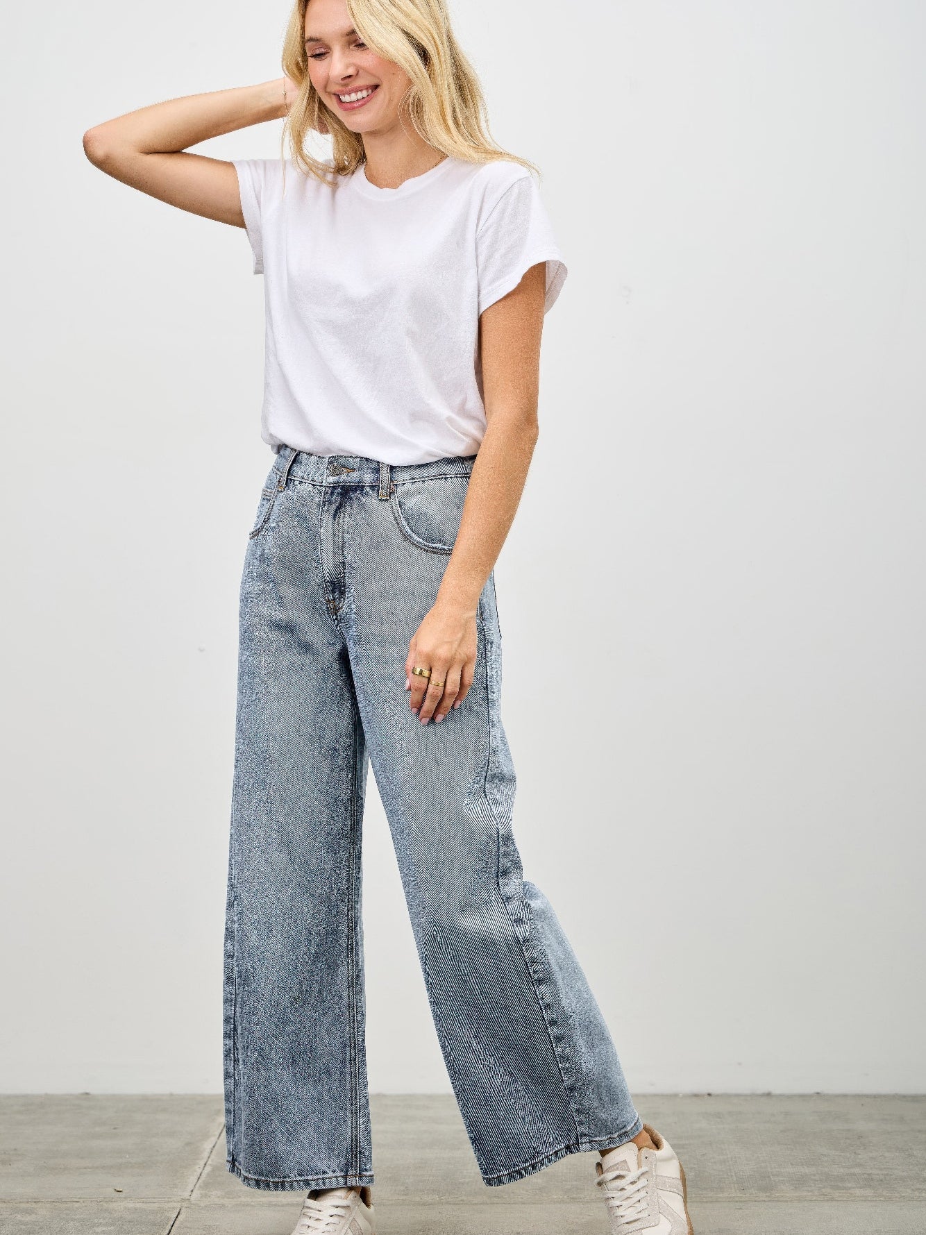 Woman wearing High Rise Low Curve Barrel jeans with a white t-shirt and sneakers, showcasing a modern and stylish silhouette.