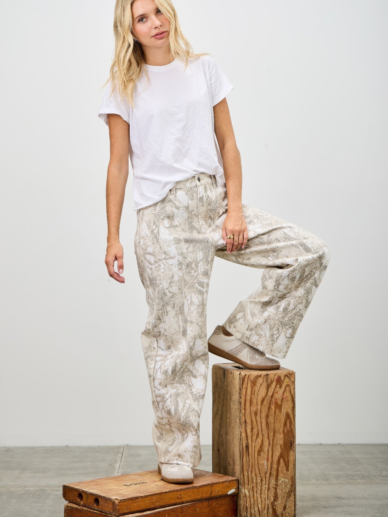 Model wearing High Rise Low Curve Barrel jeans with a white t-shirt, posing on wooden crates.