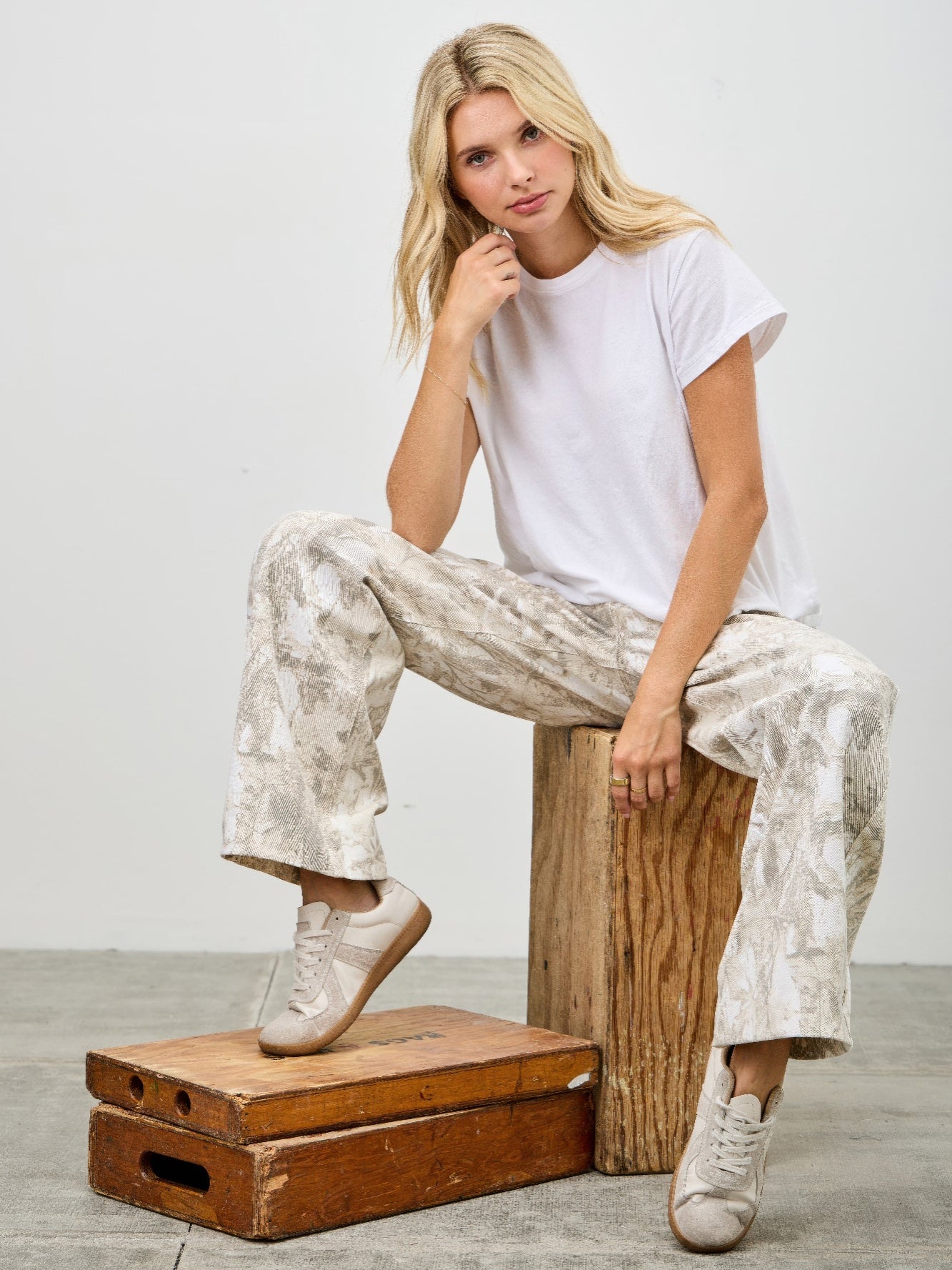Woman sitting on wooden box wearing High Rise Low Curve Barrel jeans and a white t-shirt with casual sneakers.