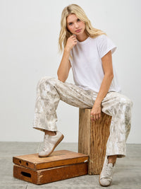 Woman sitting on wooden box wearing High Rise Low Curve Barrel jeans and a white t-shirt with casual sneakers.