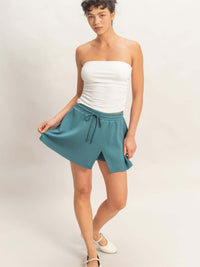Model wearing a Wrap Front Elastic Waist Skort in teal, showcasing its stylish design and comfortable fit.
