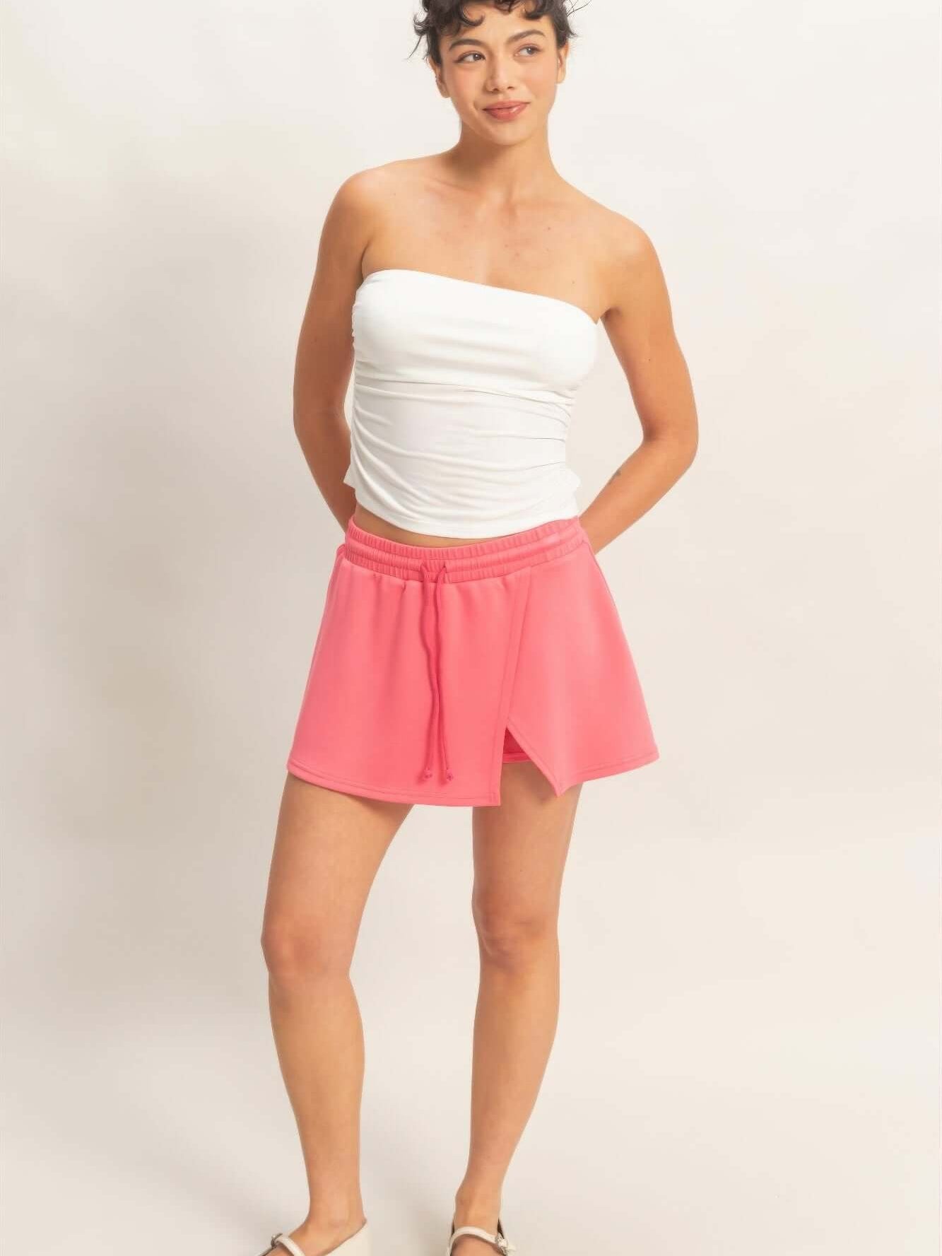 Model wearing a Wrap Front Elastic Waist Skort in vibrant pink, paired with a white strapless top.