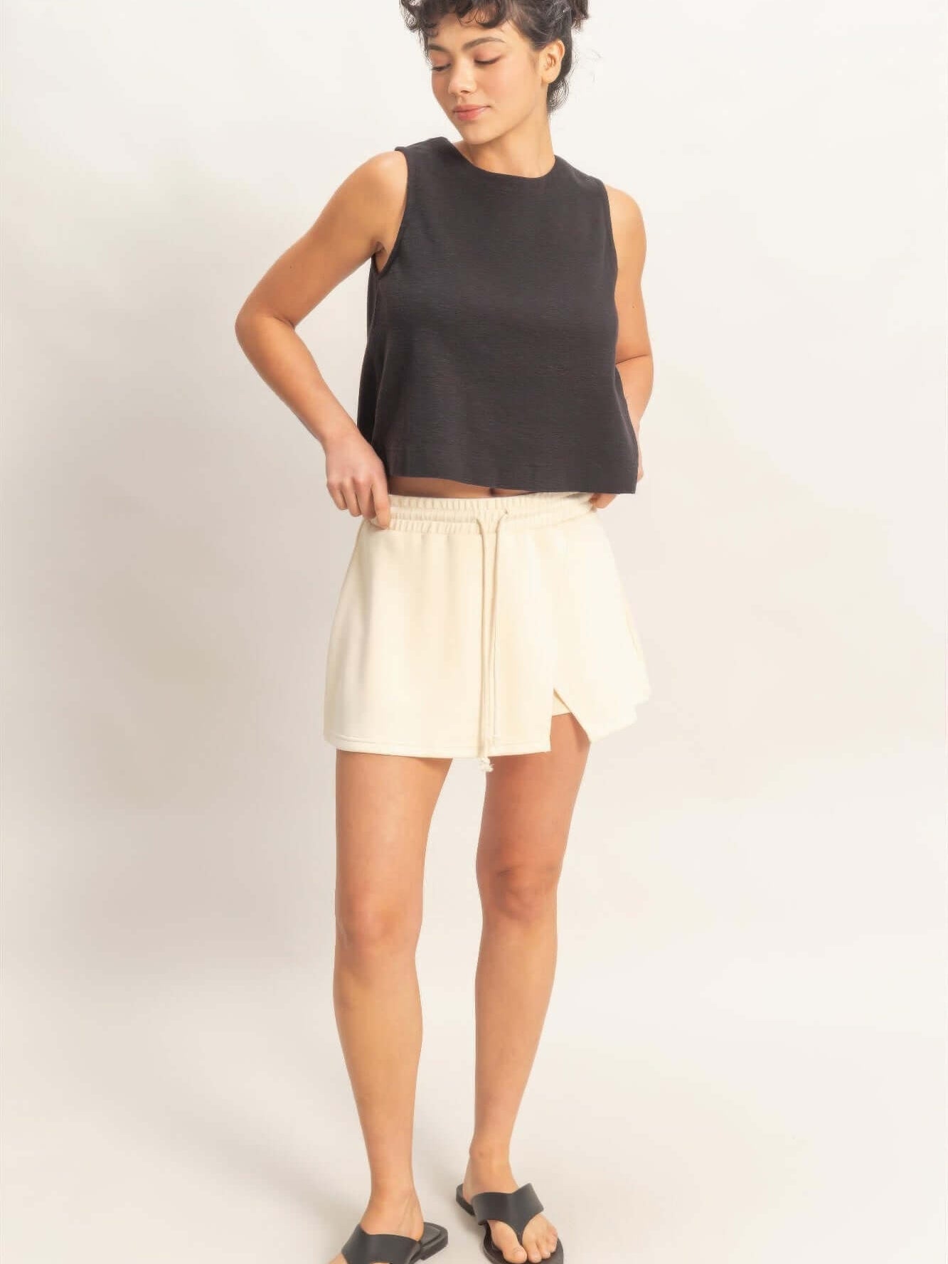 Model wearing a wrap front elastic waist skort paired with a black sleeveless top and sandals.