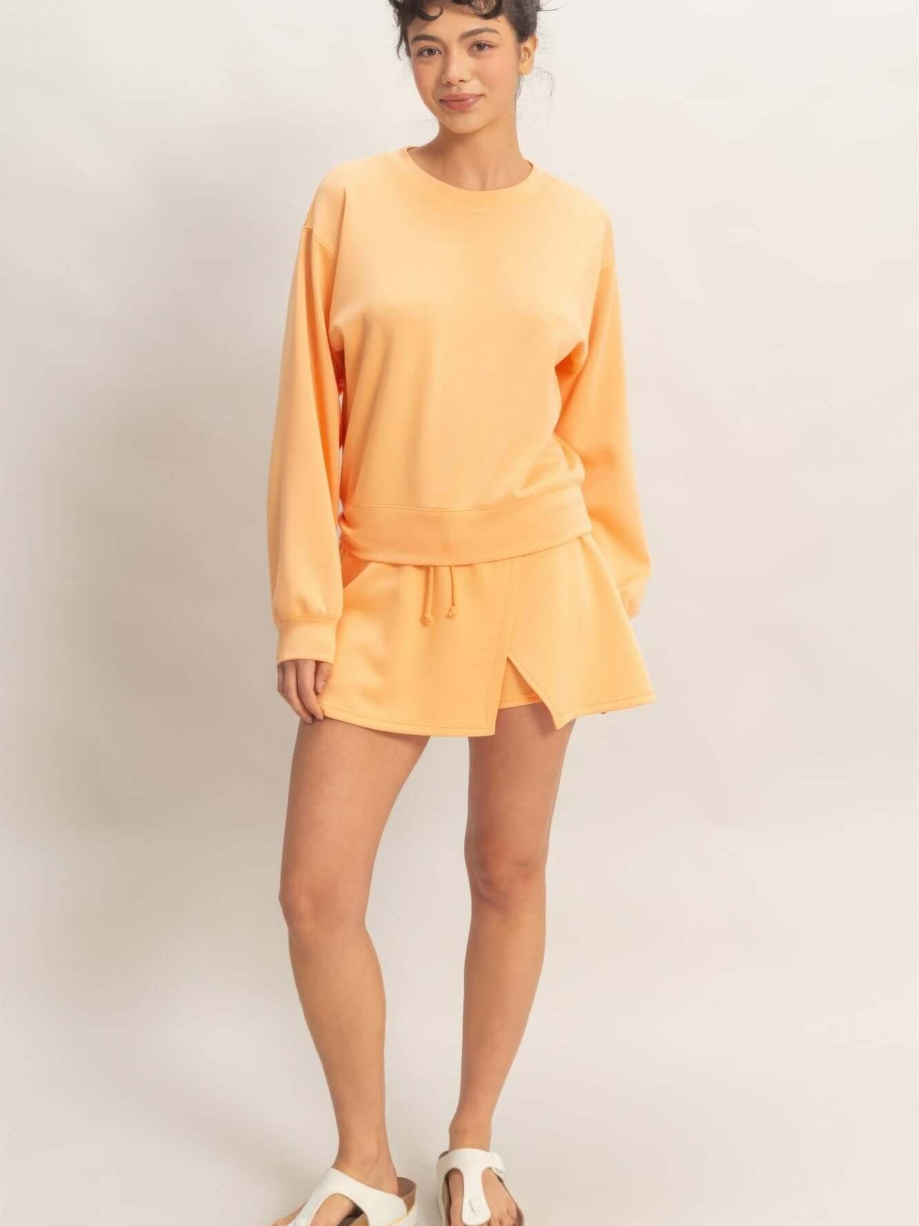 Model wearing a stylish wrap front elastic waist skort with matching sweatshirt in soft orange, showcasing casual comfort.