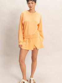 Model wearing a stylish wrap front elastic waist skort with matching sweatshirt in soft orange, showcasing casual comfort.