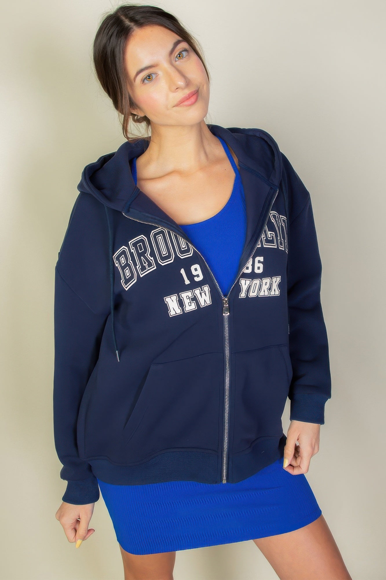 Model wearing a navy Graphic Drop Shoulder Zipper Up Hoodie with Brooklyn logo over a blue dress. Stylish and comfortable casual wear.