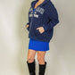 Woman modeling a navy graphic drop shoulder zipper up hoodie with Brooklyn logo, paired with a blue skirt and black knee-high boots.