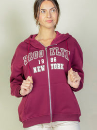 Model wearing a burgundy Graphic Drop Shoulder Zipper Up Hoodie with Brooklyn logo, perfect for casual styles.