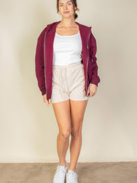 Model wearing a burgundy Graphic Drop Shoulder Zipper Up Hoodie with white tank top and beige shorts, showcasing casual style.