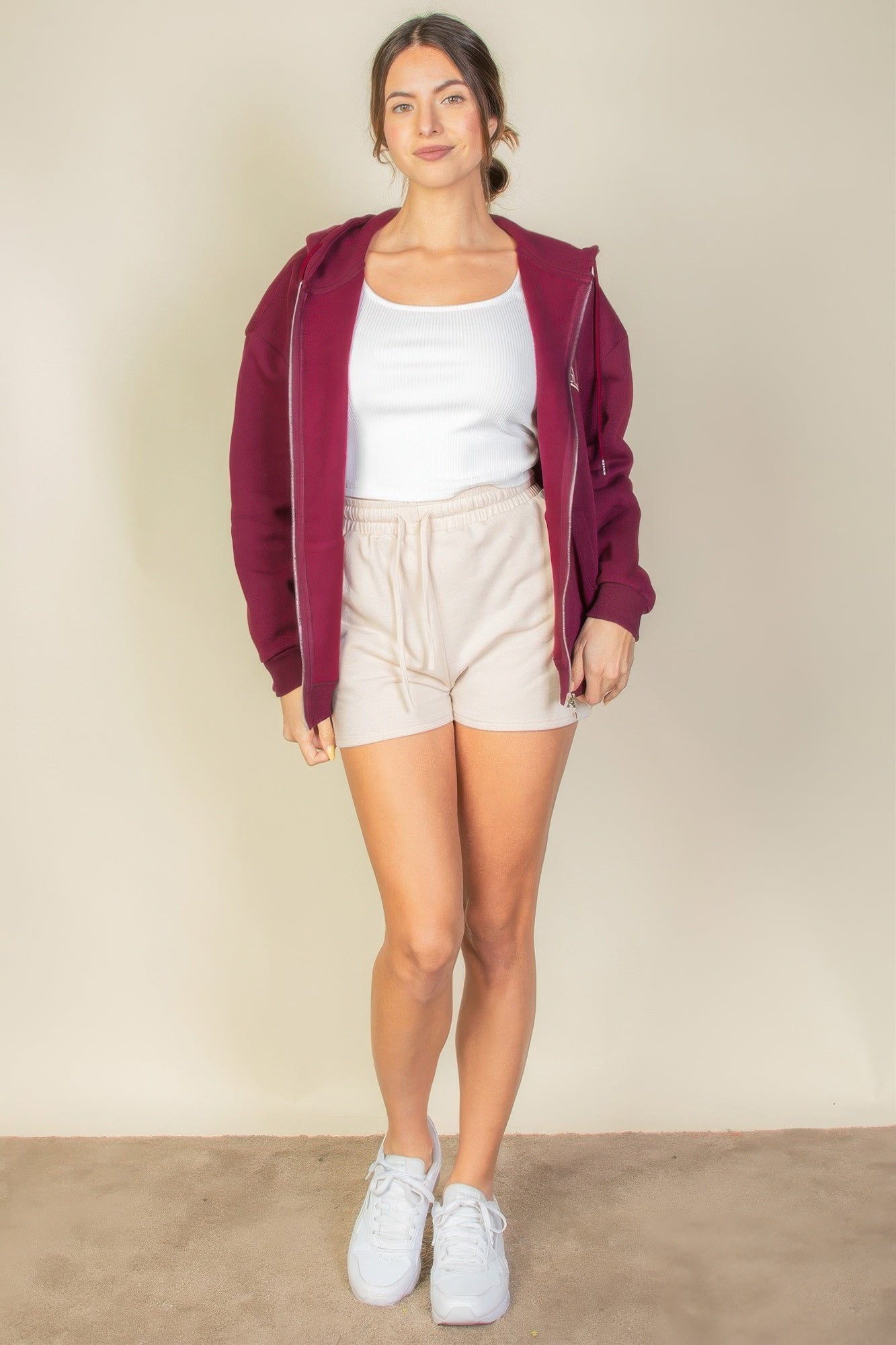 Model wearing a burgundy Graphic Drop Shoulder Zipper Up Hoodie with white tank top and beige shorts, showcasing casual style.