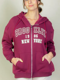 Model wearing a burgundy Graphic Drop Shoulder Zipper Up Hoodie featuring Brooklyn logo, perfect for casual style.