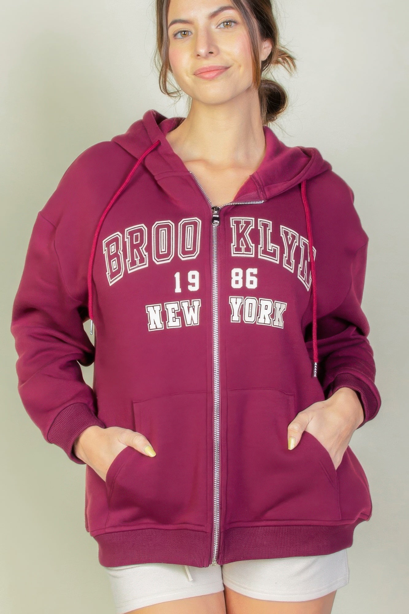 Model wearing a burgundy Graphic Drop Shoulder Zipper Up Hoodie featuring Brooklyn logo, perfect for casual style.