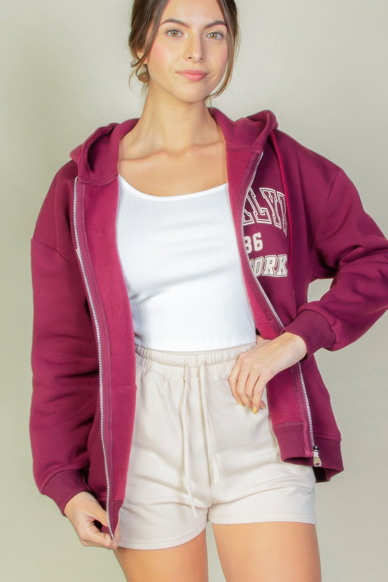 Model wearing a maroon Graphic Drop Shoulder Zipper Up Hoodie over a white tank top and beige shorts.