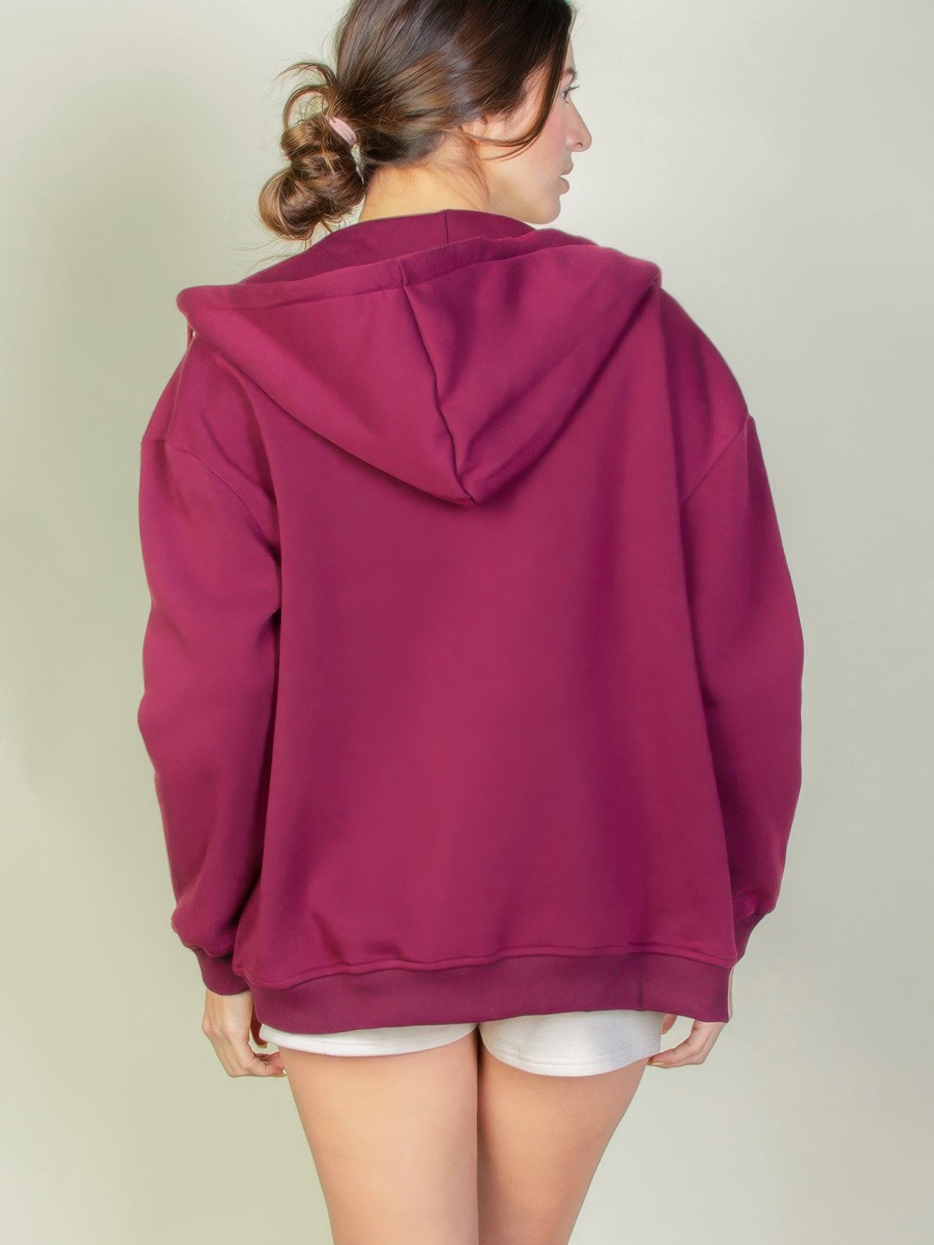 Back view of a burgundy graphic drop shoulder zipper up hoodie against a neutral background.