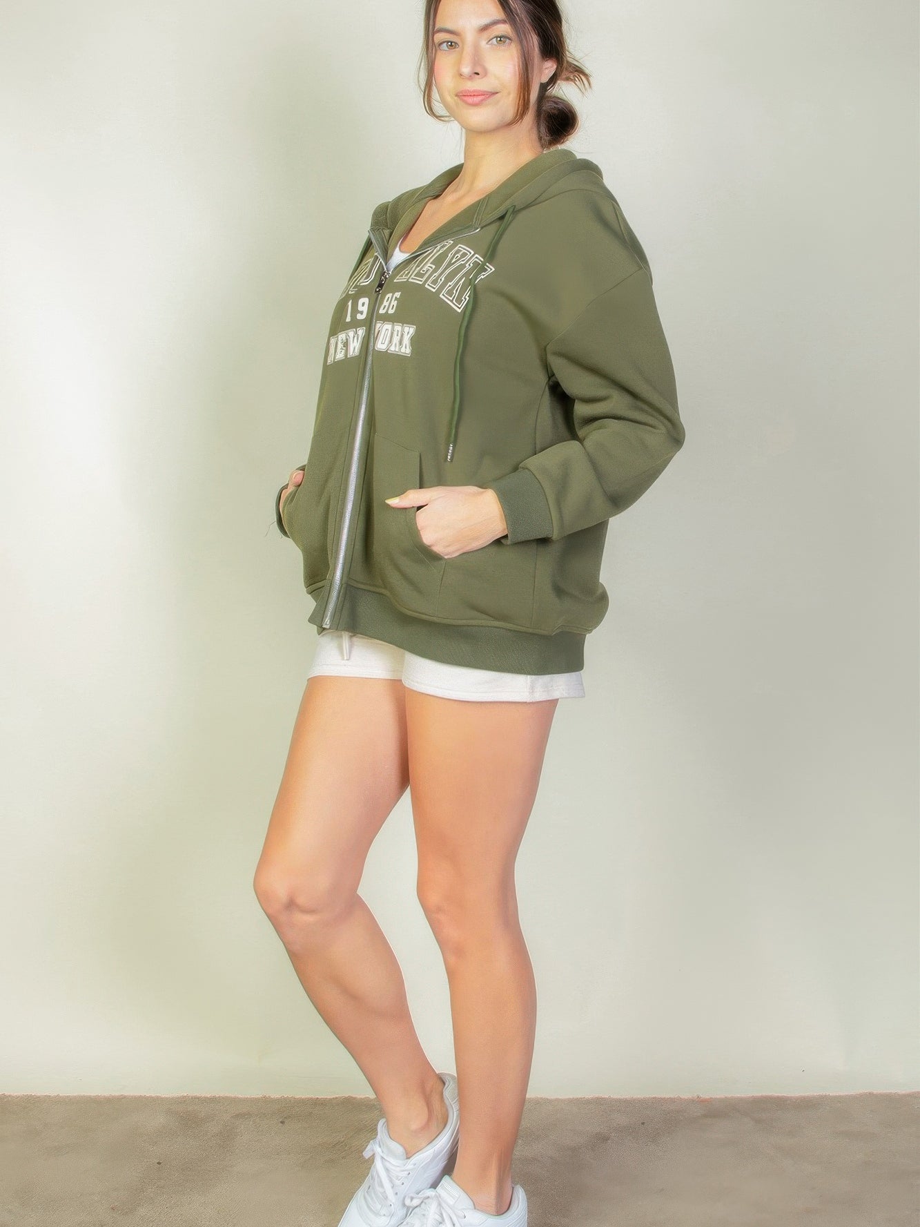 Woman wearing a Graphic Drop Shoulder Zipper Up Hoodie, featuring a Brooklyn logo and soft, stretchy fabric for comfort.