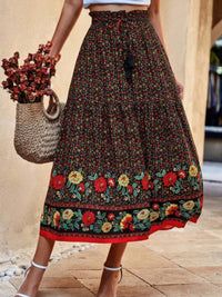 Drawstring Floral Ruffled Maxi Skirt in black floral print, featuring ruffles and a drawstring waist, styled with a woven bag.