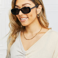 Woman wearing Oval Full Rim Sunglasses, featuring a stylish look with gold accessories.