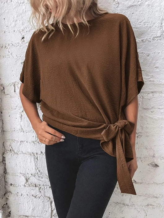 Knotted Round Neck Half Sleeve Blouse in brown worn with black jeans, showcasing its tied design on a model.